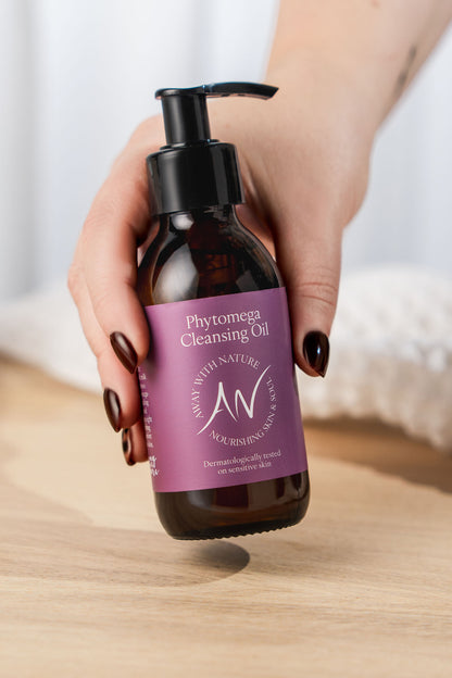 Hand holding Phytomega Cleansing Oil with Borage and Frankincense in an amber pump bottle with a plum label